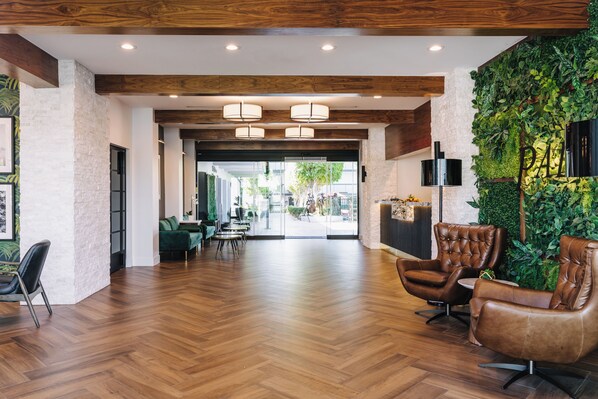 A spacious lobby with wooden flooring, leather armchairs, a reception desk, and a green wall with plants. - Palm Garden Hotel (Thousand Oaks)