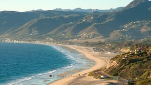 A coastal landscape with a beach, houses, and hills in the background. - Palm Garden Hotel (Thousand Oaks)