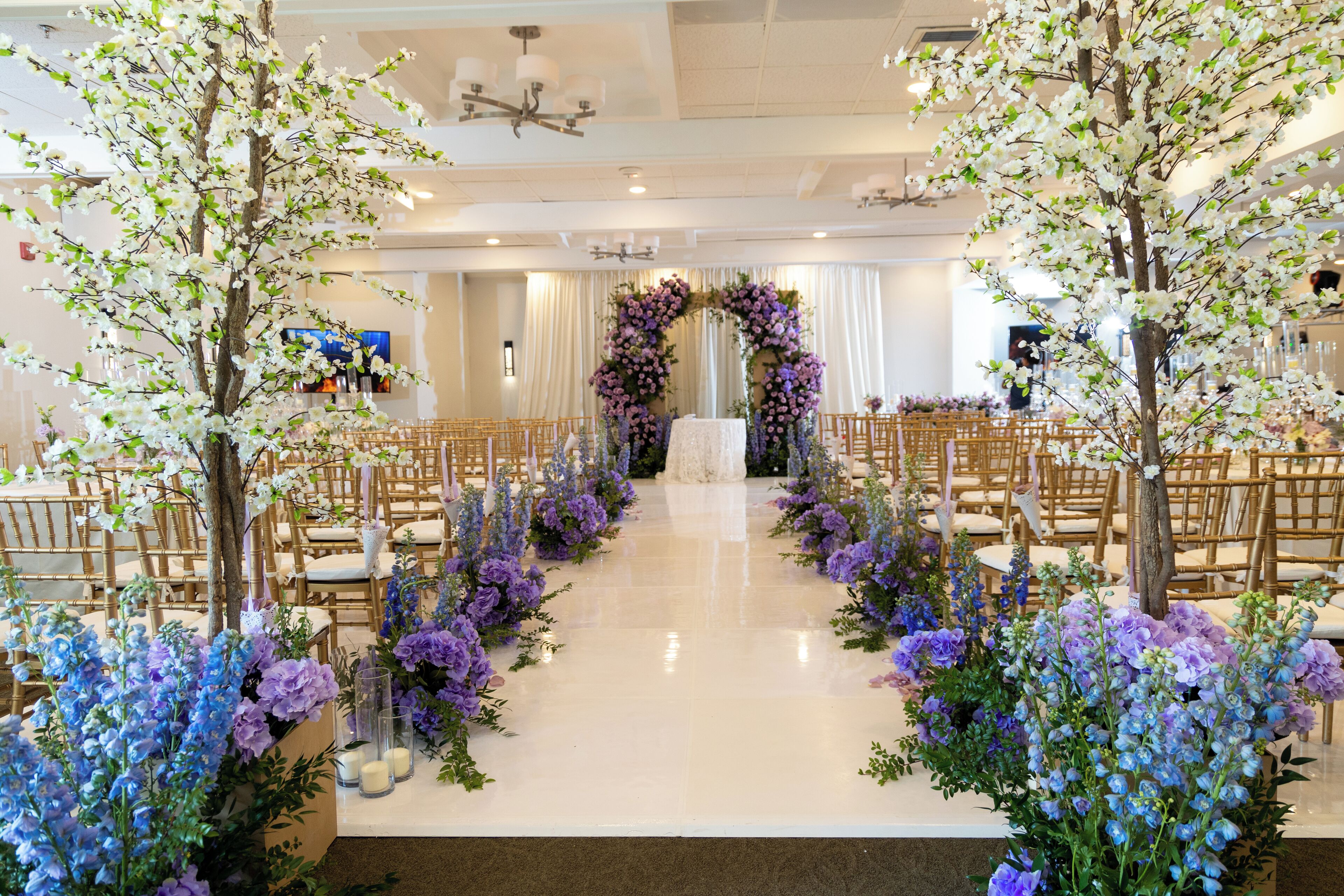 Um local de casamento com um corredor branco, decoração floral e cadeiras de madeira.