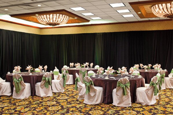 A banquet hall with round tables, chairs with green sashes, and a chandelier.
