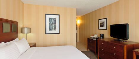A hotel room with a bed, a television, a dresser, and two framed pictures on the wall.