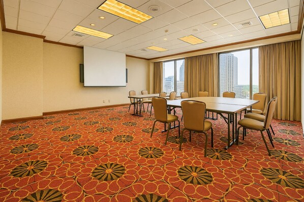 A conference room with a large table, chairs, a projector screen, and a carpet with a floral pattern. - Holiday Inn Sacramento Downtown-Arena by IHG (Sacramento)