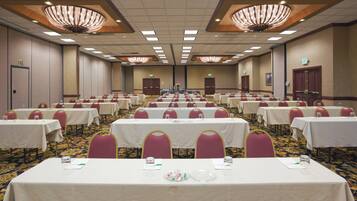 Un amplio salón de conferencias con varias mesas y sillas, candelabros e instalación de alfombra.
