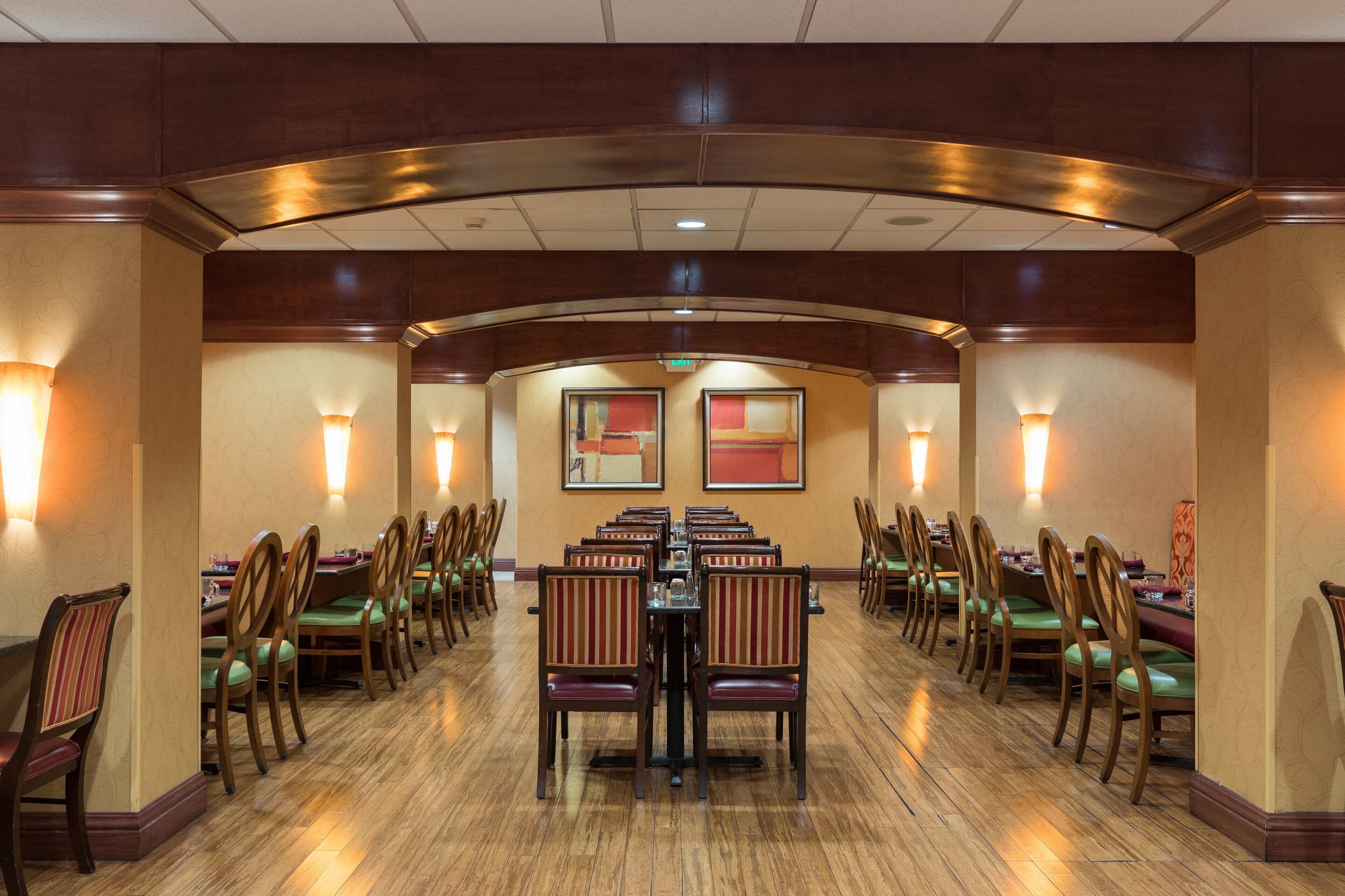 A conference room with rows of tables and chairs, equipped with wall-mounted lamps and framed artwork.