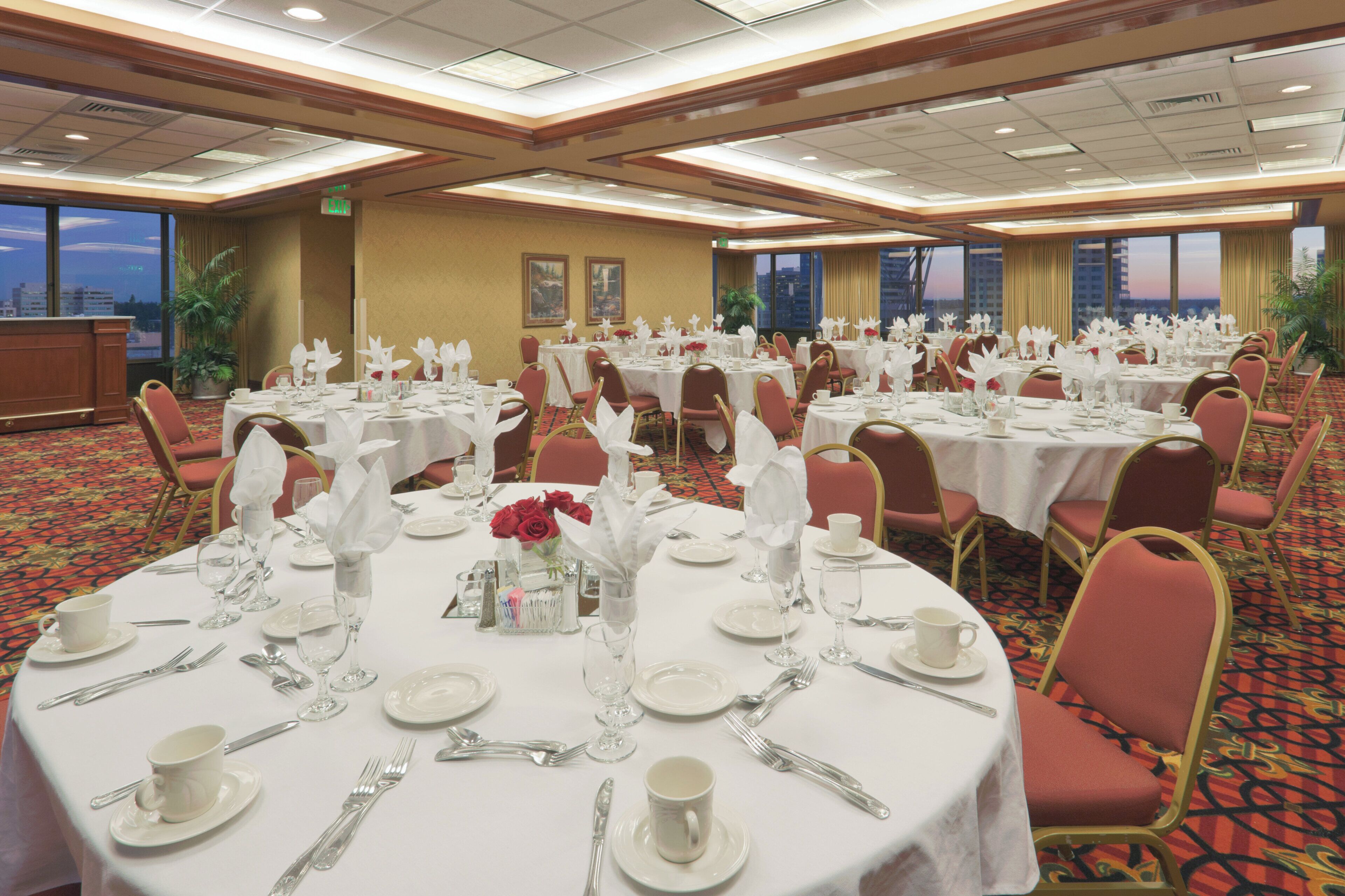 A banquet hall with round tables set for dining, featuring white tablecloths, red chairs, and floral centerpieces.