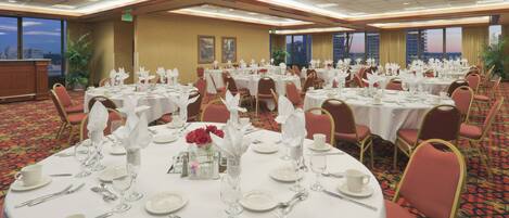 A banquet hall with round tables set for dining, featuring white tablecloths, red chairs, and floral centerpieces.