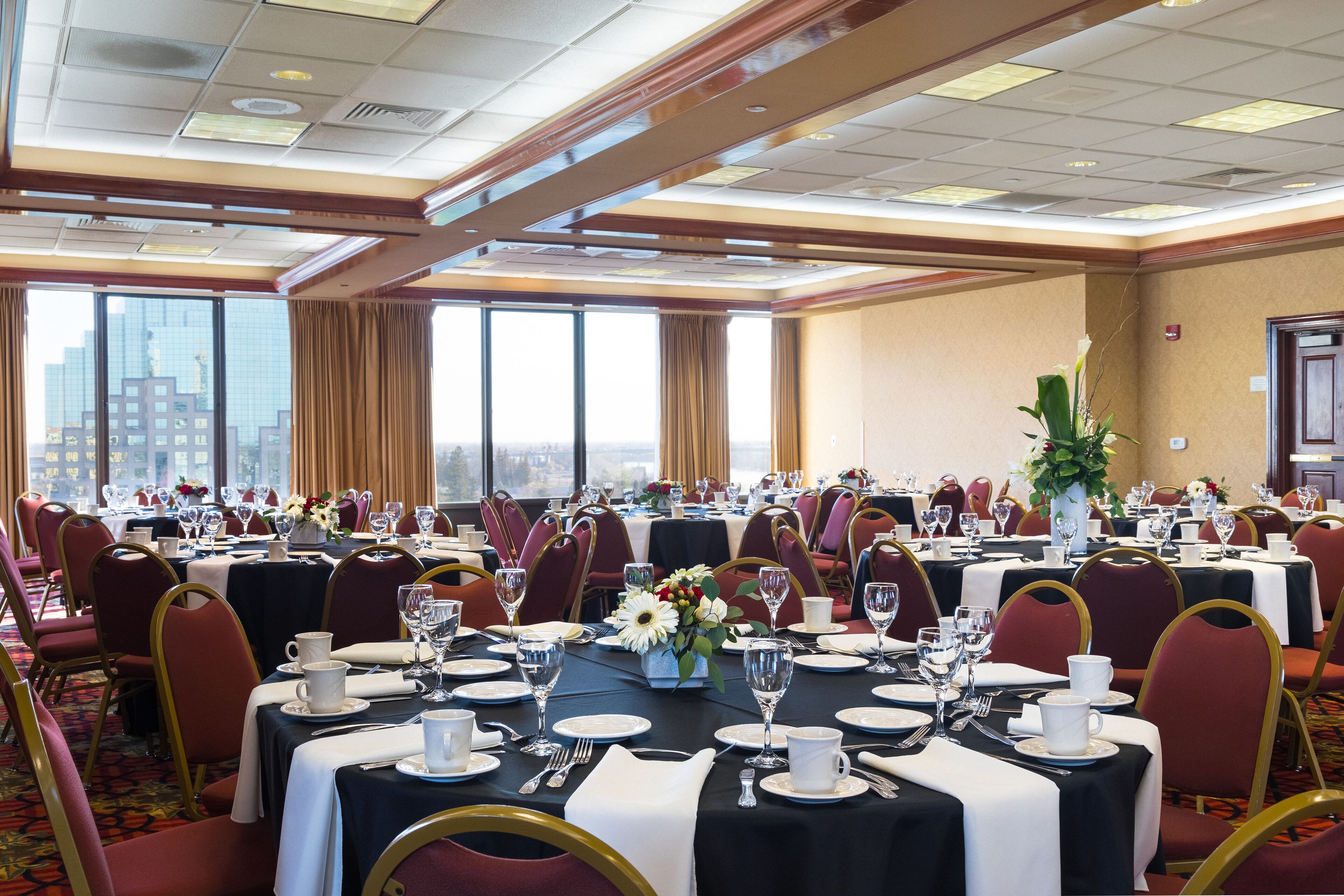 A banquet hall with round tables set for dining, large windows, and a city view.
