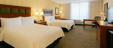 A hotel room with two beds, a desk, a television, and a window with curtains.