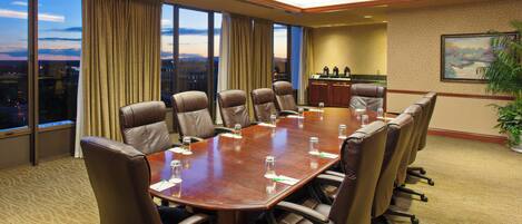 A conference room with a large table, multiple chairs, a view of the cityscape through large windows, and a painting on the wall.