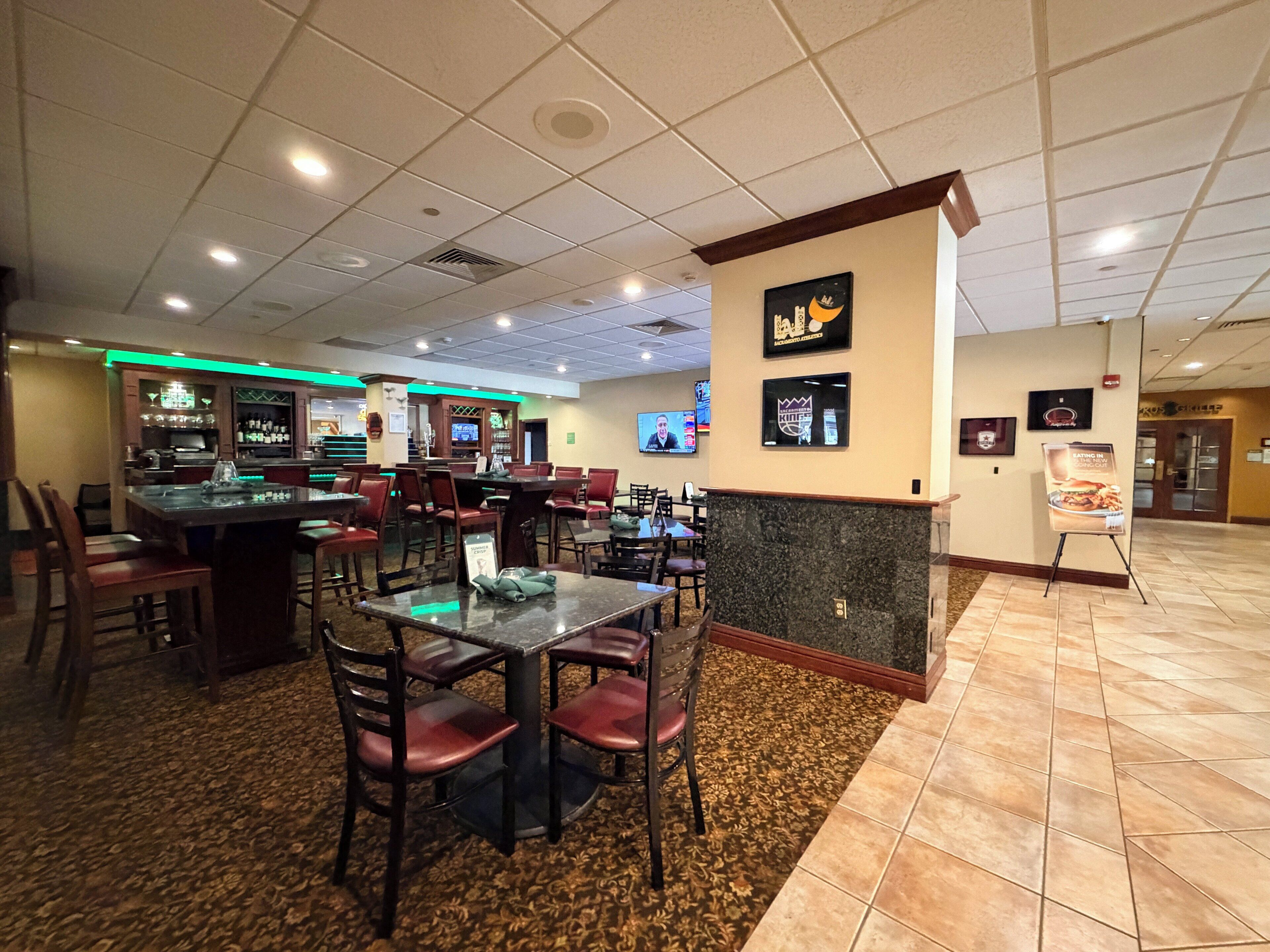 A restaurant with multiple tables and chairs, a bar area, and a television screen.