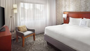 Una habitación de hotel con una cama grande, una silla, un escritorio y una lámpara.