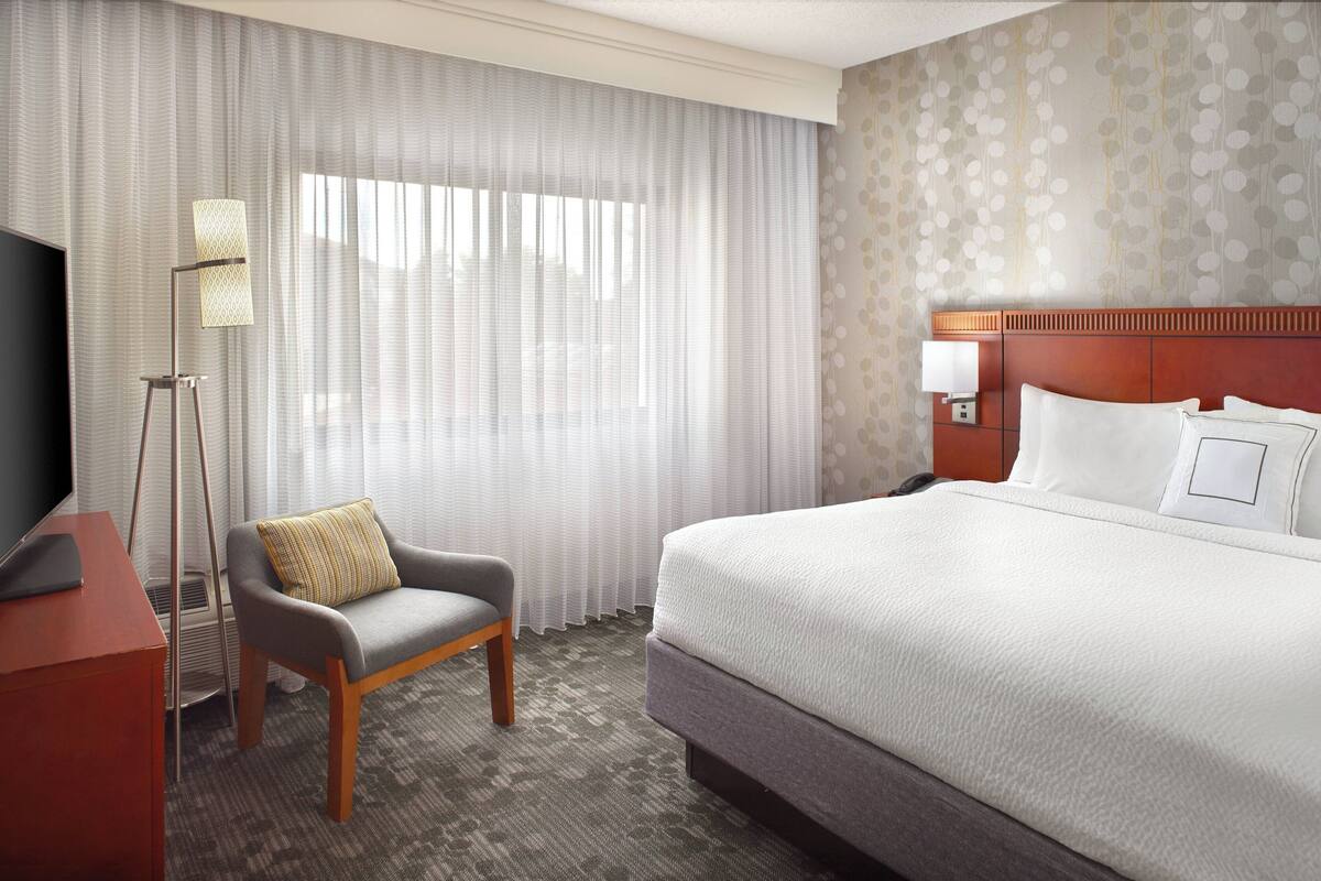 Una habitación de hotel con una cama grande, una silla, un escritorio y una lámpara.