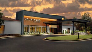 Entrada moderna de un hotel con el letrero 'Courtyard by Marriott', un camino cubierto y zonas ajardinadas.