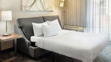 Een moderne hotelkamer met een groot bed, een nachtkastje met een lamp, een vloerlamp en een groot abstract schilderij aan de muur.