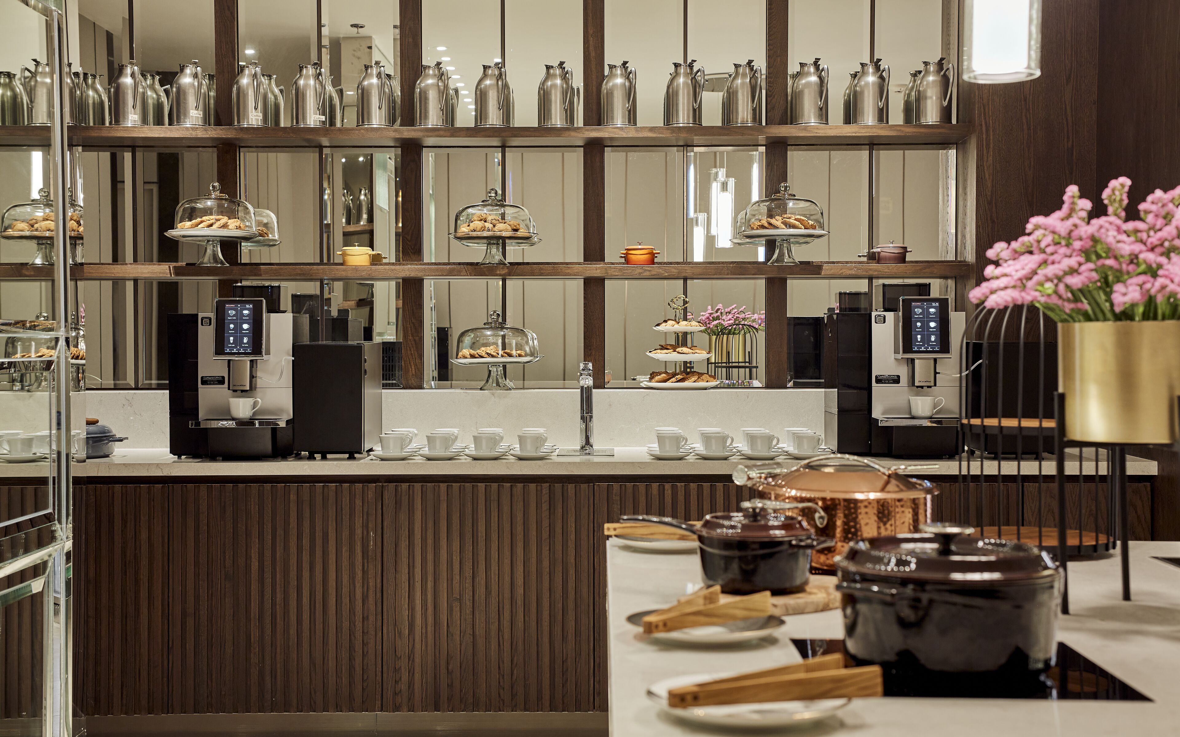 A modern coffee station with multiple coffee machines, a display of pastries, and a decorative vase of flowers.