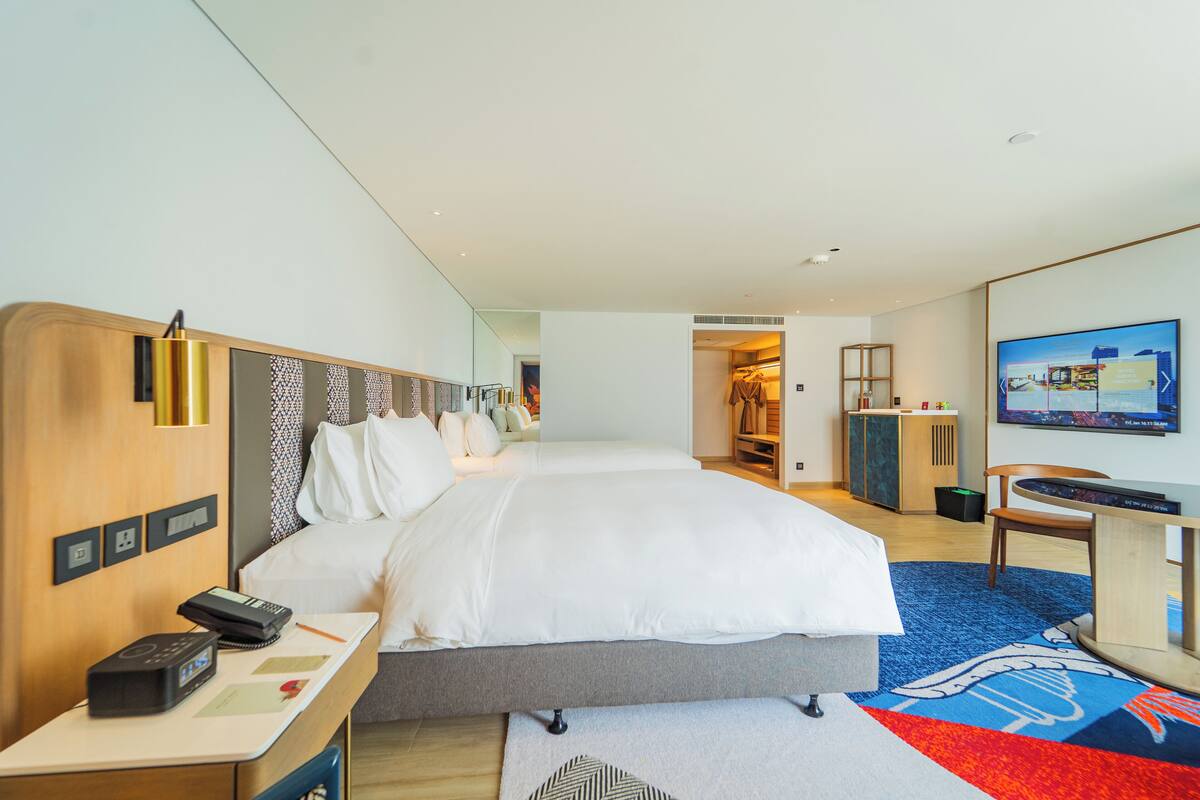 A hotel room with a large bed, bedside table with a phone, a desk with a chair, a TV, and a wardrobe.