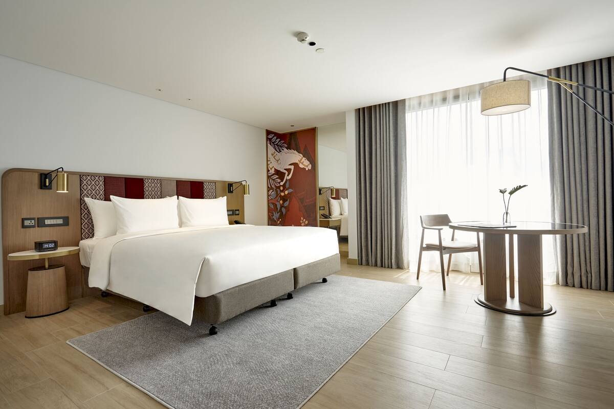 A modern hotel room with a bed, bedside table, lamp, and a round table with chairs.