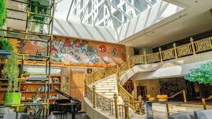 A spacious lobby with a grand staircase, a piano, and a mural. - Montien Hotel Surawong Bangkok (Bangkok)