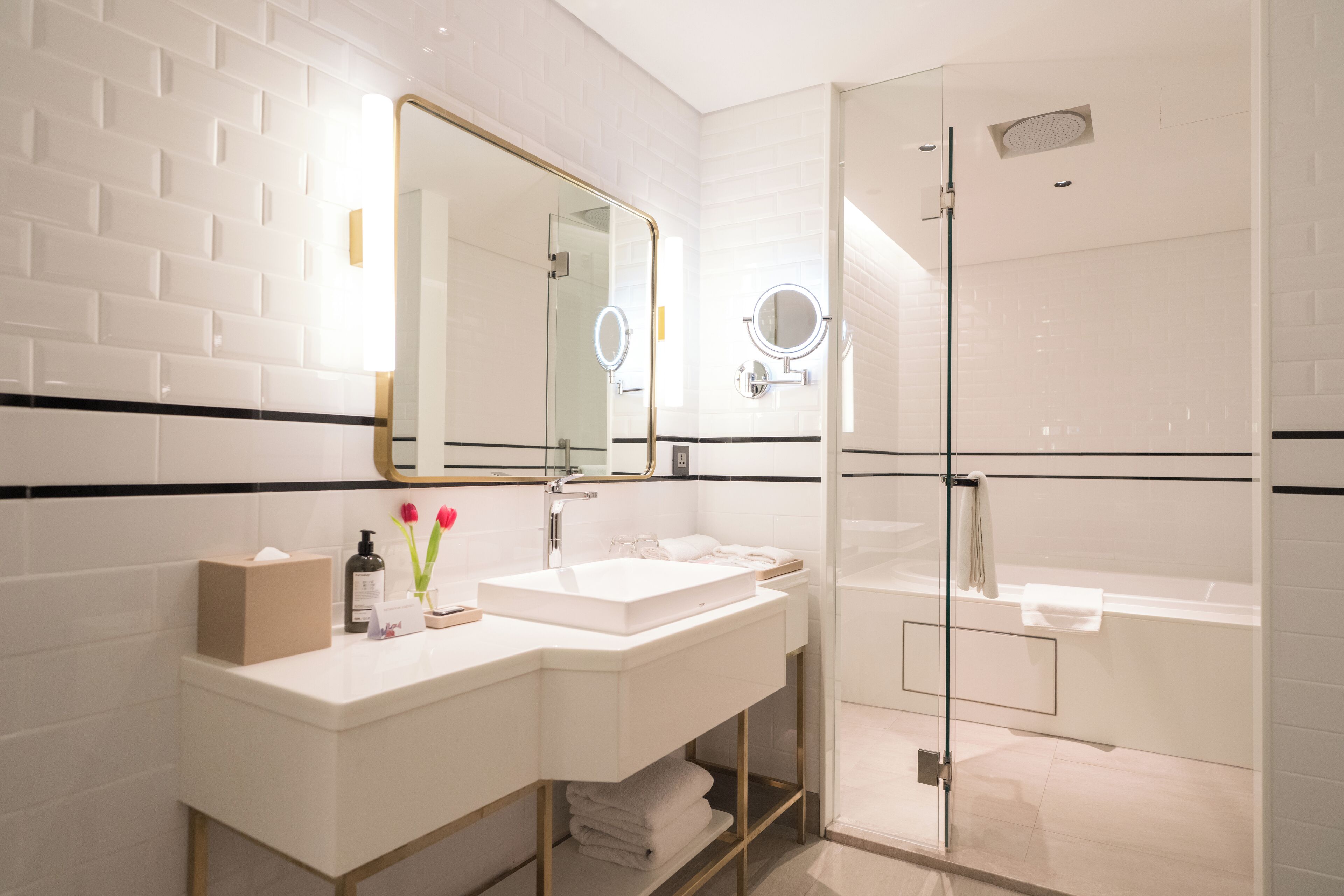 A modern bathroom with a white sink, mirror, and glass shower enclosure.