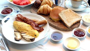 Un desayuno abundante con huevos, tocino, tostadas, croissants y diversas frutas y salsas.