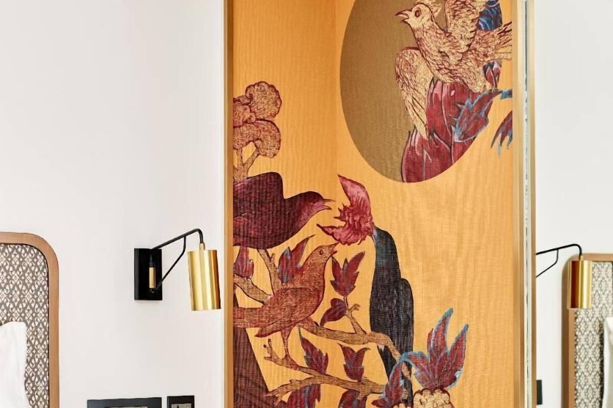 A hotel room with a bed, bedside table, lamp, phone, and a decorative wooden partition with a bird and floral design.