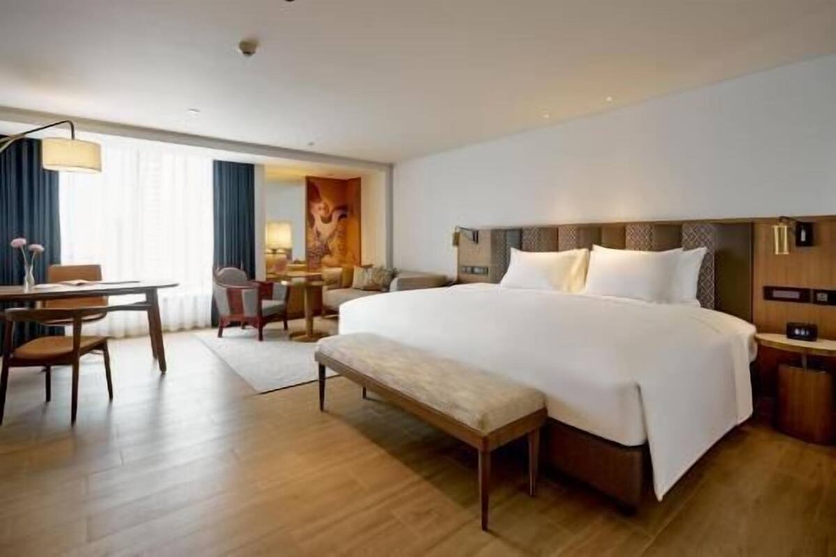 A hotel room with a large bed, a desk, a chair, and a bench.