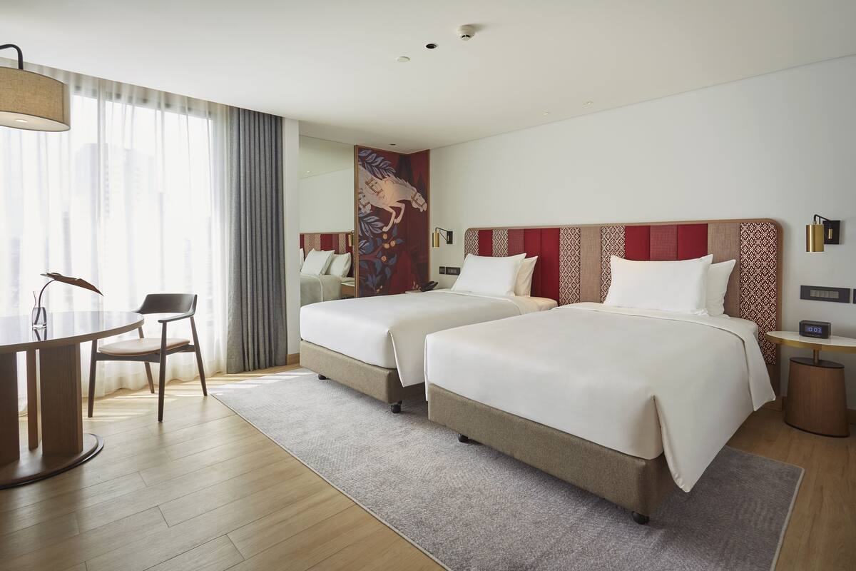 A hotel room with two beds, a desk, and a chair.
