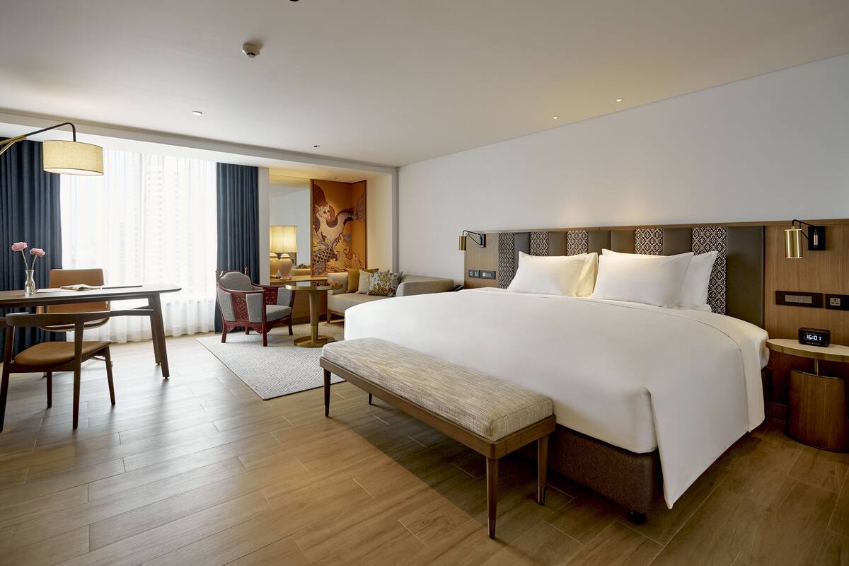 A hotel room with a large bed, a desk, a chair, and a bench.