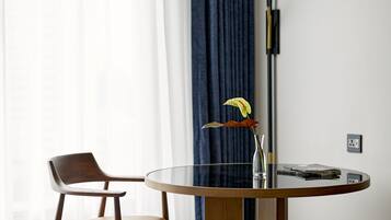 Una habitación moderna con una mesa redonda de vidrio, una silla de madera, una lámpara de pie y un florero con una flor.