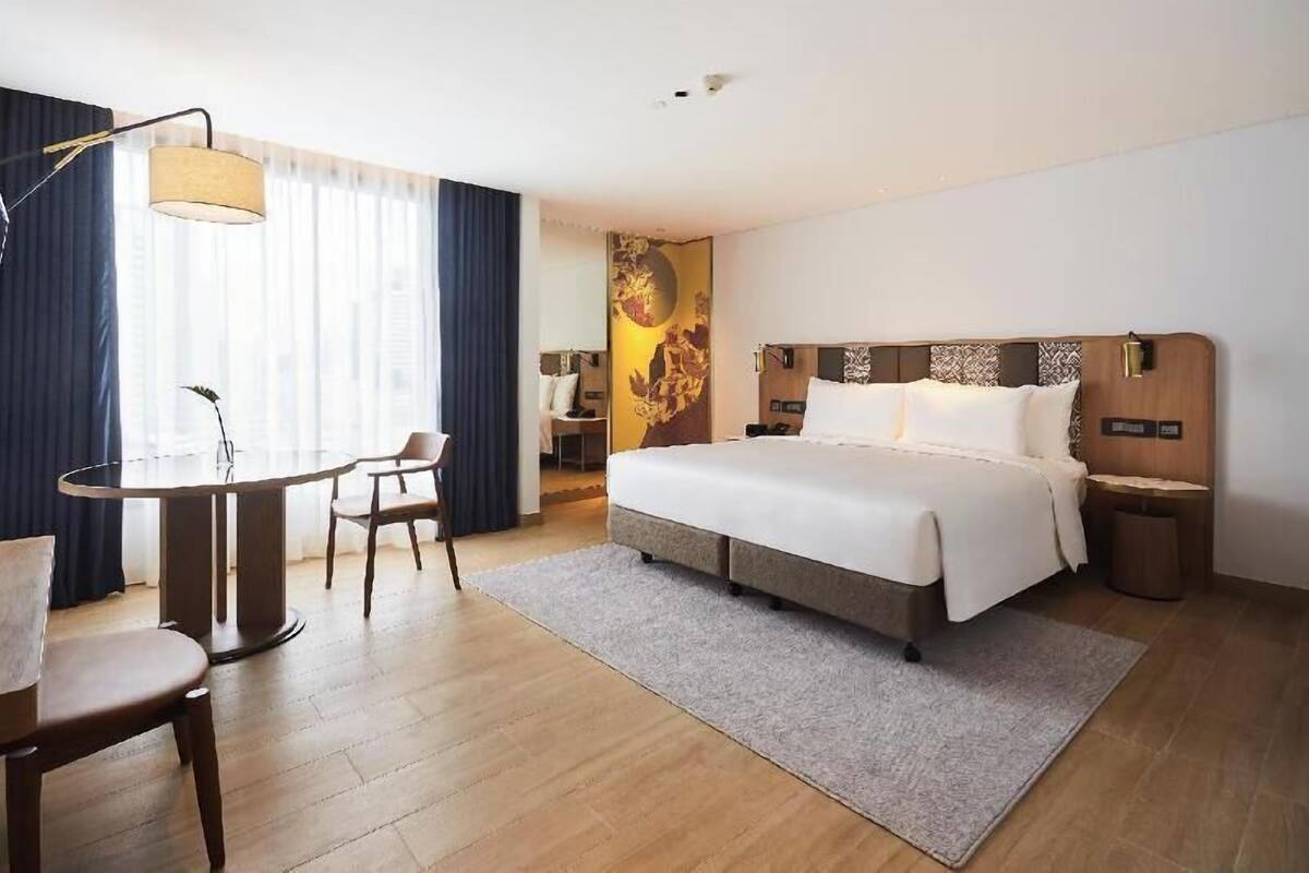A hotel room with a bed, a round table with chairs, a lamp, and a wall with a decorative panel.