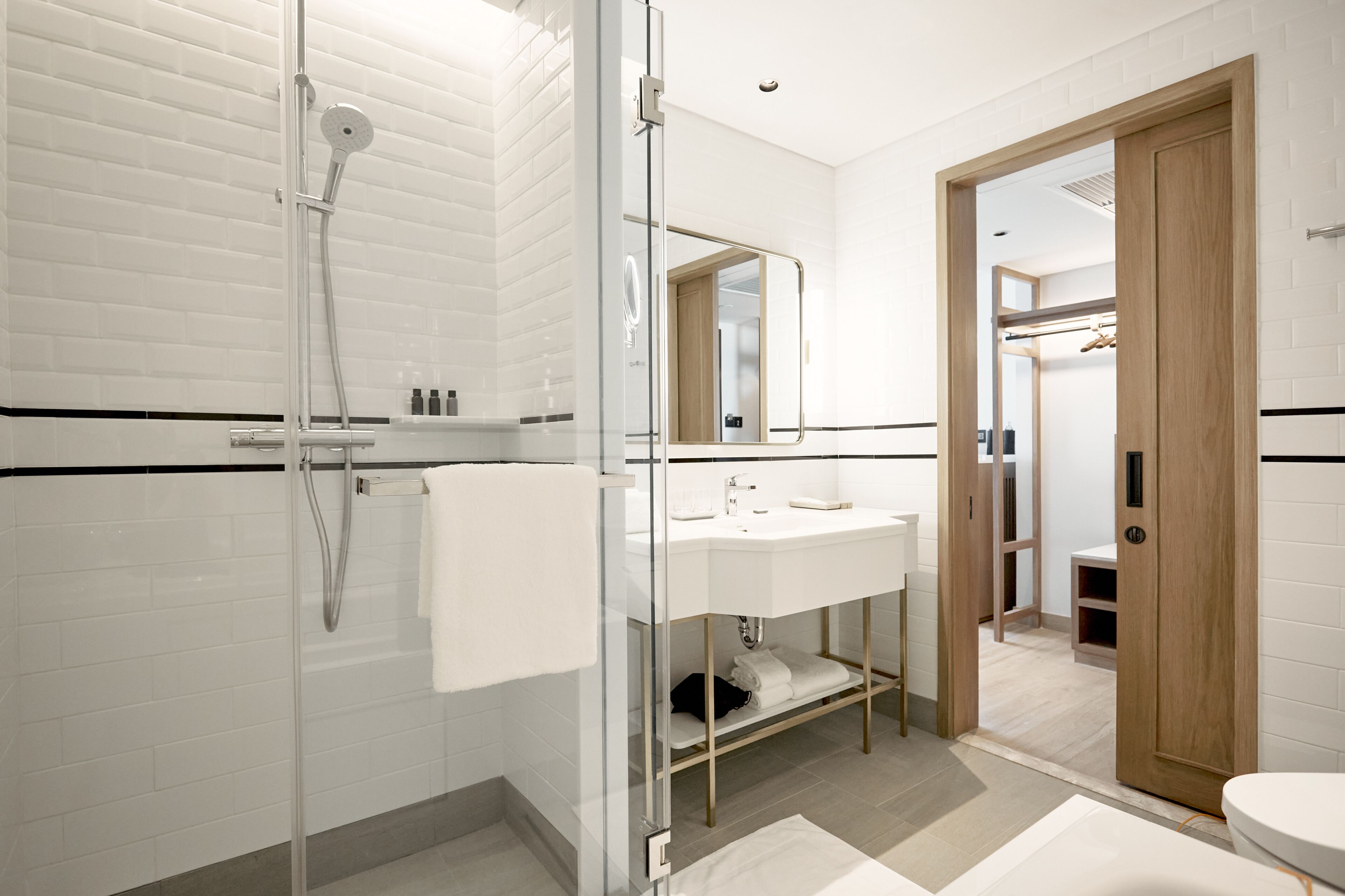 A modern bathroom with a glass-enclosed shower, a white sink with a mirror above it, and a wooden door leading to another room.