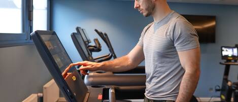 A man using a treadmill with a digital display, in a room with exercise equipment and a TV.