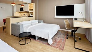 Et moderne hotelværelse med seng, skrivebord, fjernsyn, tekøkken og badeværelse.