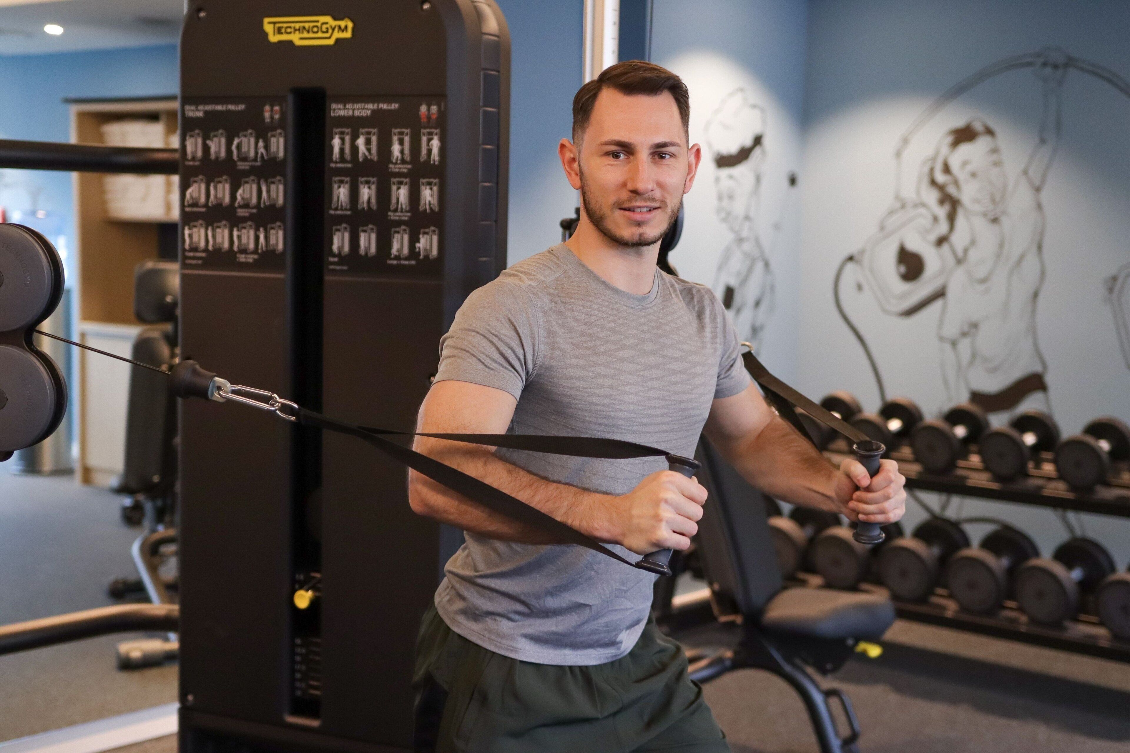 Ein Fitnessstudio mit Trainingsgeräten, darunter ein Kabelzuggerät und Kurzhanteln.