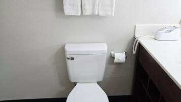 Um banheiro com vaso sanitário branco, um porta-toalhas com toalhas enroladas e um suporte de papel higiênico branco.