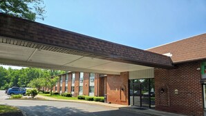 A building with a covered entrance, brick facade, and a parking lot with cars. - Fulton Hotel - Oswego Riverfront (Fulton)