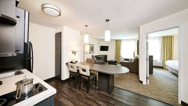 A modern hotel room with a kitchenette, a dining area, a seating area, and a bed.