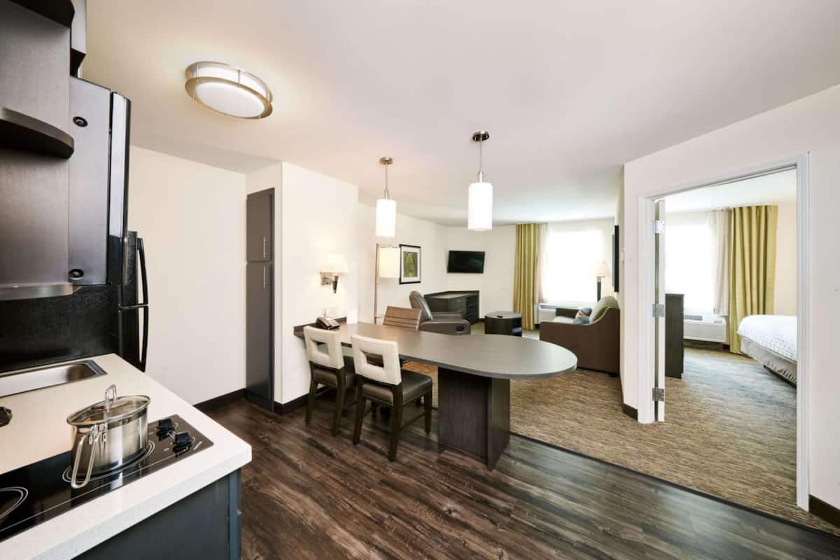 Una habitación de hotel moderna con kitchenette, zona de comedor, sala de estar y cama.