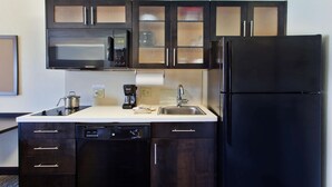 A compact kitchen with dark cabinetry, a black refrigerator, a microwave, a dishwasher, and a coffee maker.