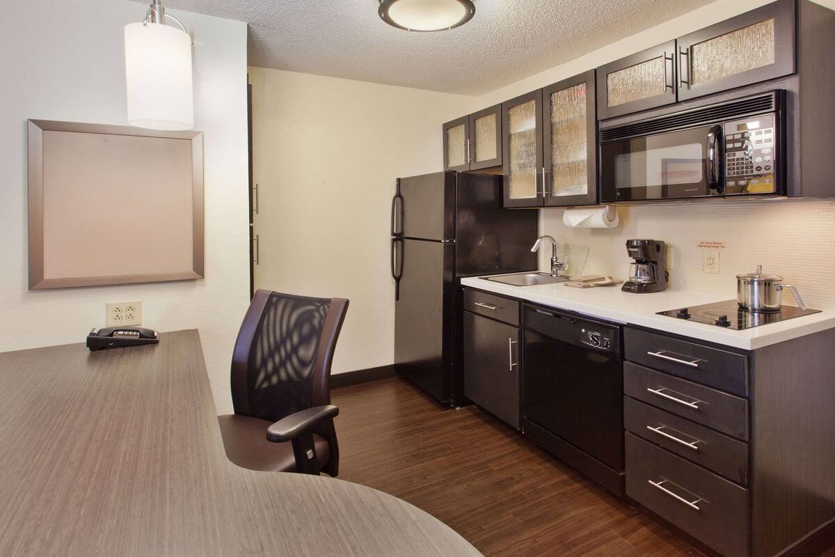 Una cocina moderna con microondas integrado, refrigerador y lavavajillas. Hay una mesa de comedor con sillas y una lámpara colgante arriba.
