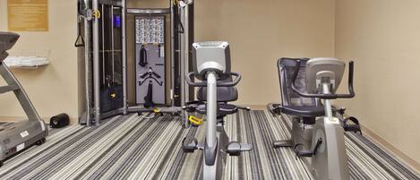 A gym with cardio machines, weight machines, and a wall-mounted rack of dumbbells.