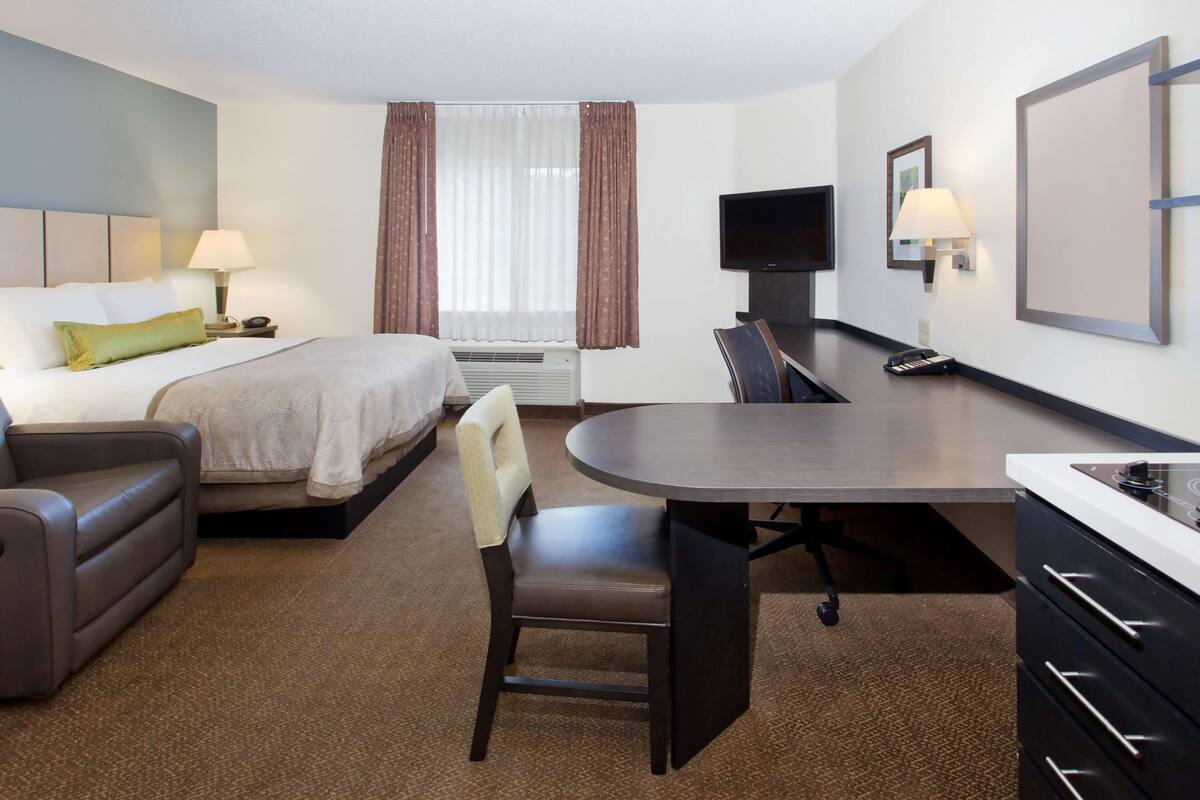 Una habitación de hotel con una cama, un escritorio, una silla, un televisor y una lámpara.