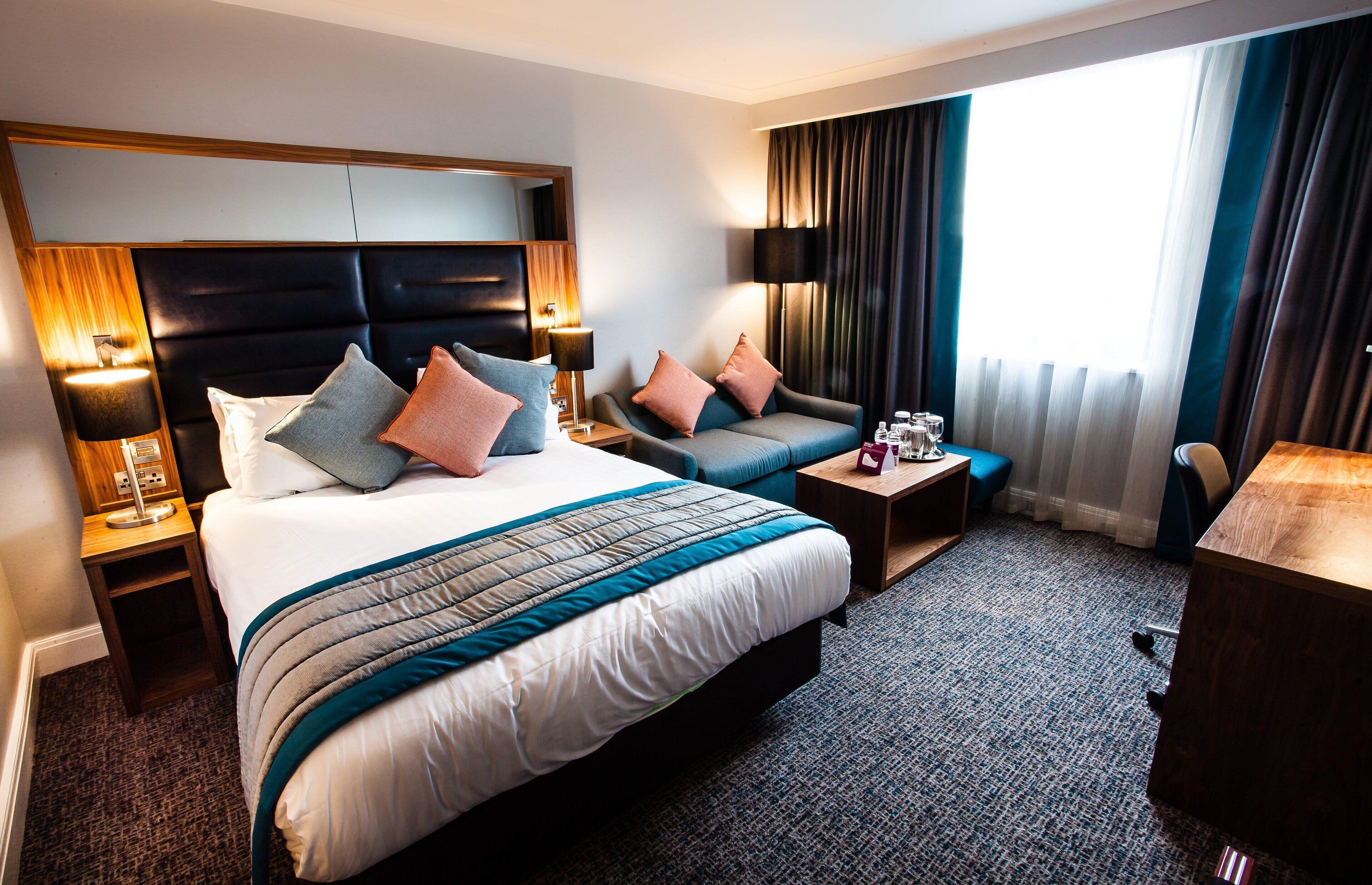 Ein Hotelzimmer mit einem großen Bett, einer Couch, einem Schreibtisch und einem Fenster mit Vorhängen.