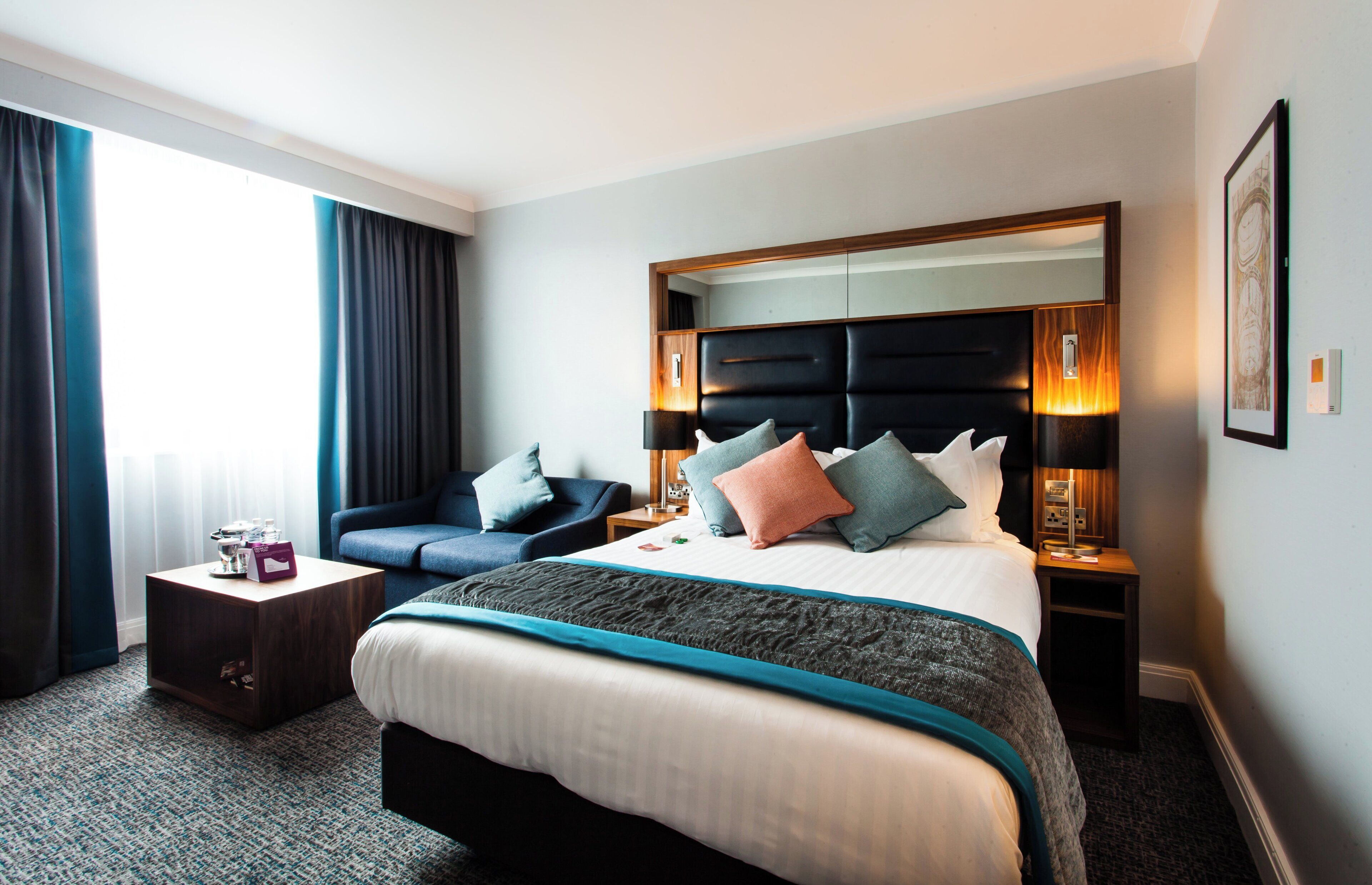 Ein Hotelzimmer mit einem großen Bett, einem Schlafsofa, einem Nachttisch und einem Fenster mit Vorhängen.