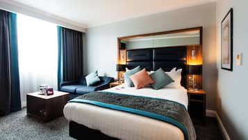 Ein Hotelzimmer mit einem großen Bett, einem Schlafsofa, einem Nachttisch und einem Fenster mit Vorhängen.