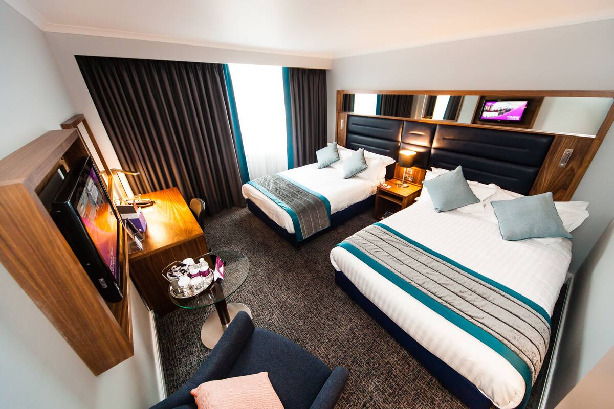 A hotel room with two beds, a TV, a desk with a computer, and a chair.