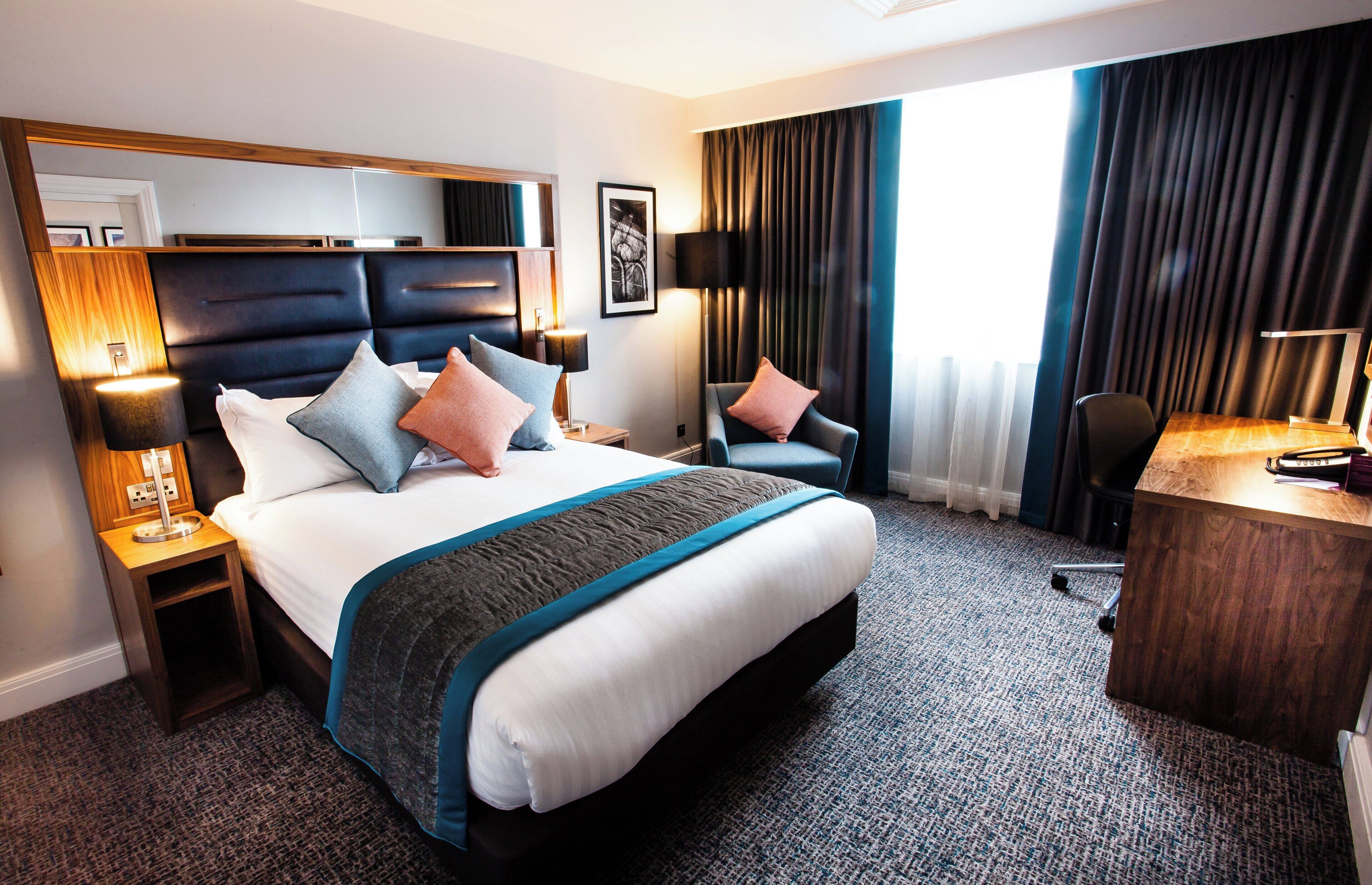 A hotel room with a large bed, a desk, a chair, and a view of the outdoors.
