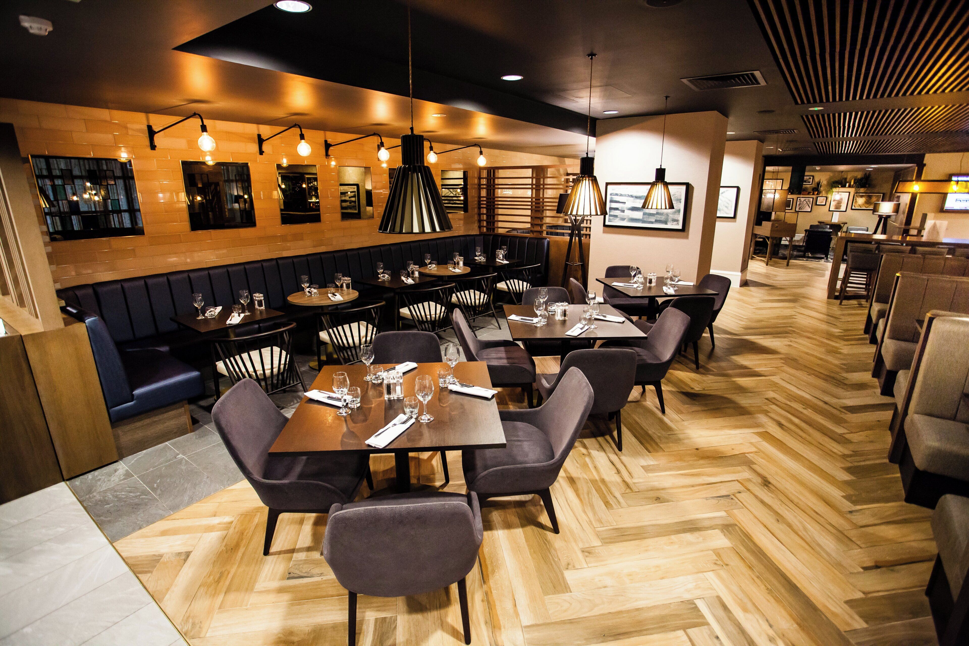 A restaurant interior with booths, tables, and a herringbone wood floor.
