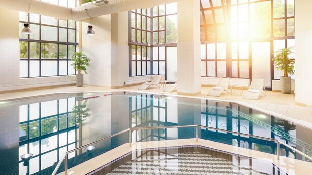 An indoor swimming pool with clear glass walls, lounge chairs, and potted plants. - Crowne Plaza Leeds by IHG (Leeds)