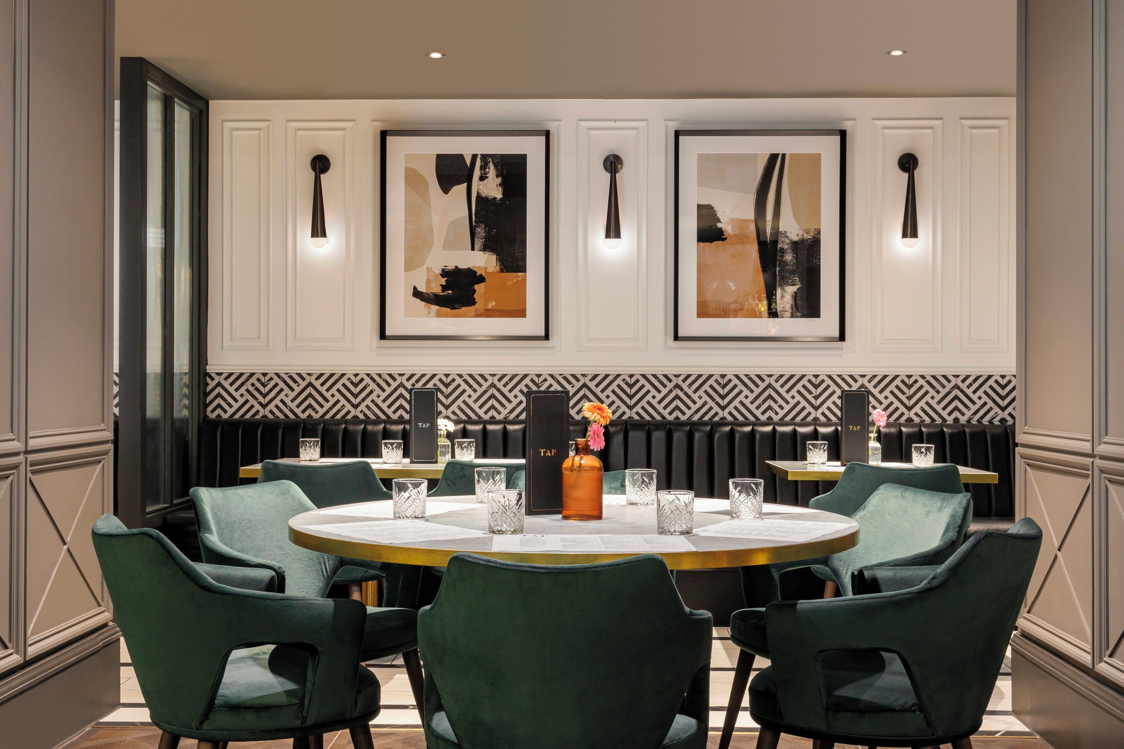 Un coin repas avec une table ronde, des chaises à revêtement vert et des œuvres d’art encadrées accrochées au mur.